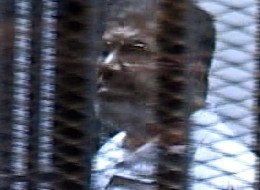 Ousted Egyptian president Mohammed Morsi is seen inside the glass cage for the first time as the prosecutor began to read out the defendants' names after Morsi and other defendants arrived at Cairo's Police Academy to attend the first session of their trial on charges of breaking out of prison during Egypt's 2011 uprising in Cairo, Egypt, on January 28, 2014. (Photo by Pool/Anadolu Agency/Getty Images)