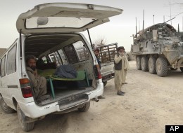 An armored military vehicle from the NATO-led International Security Assistance Force (ISAF) is seen at right, as the covered body of a person who was allegedly killed by a U.S. service member is seen inside a minibus in Panjwai, Kandahar province. (AP Photo/Allauddin Khan)