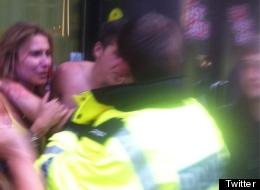 A topless Barton is restrained by a policeman